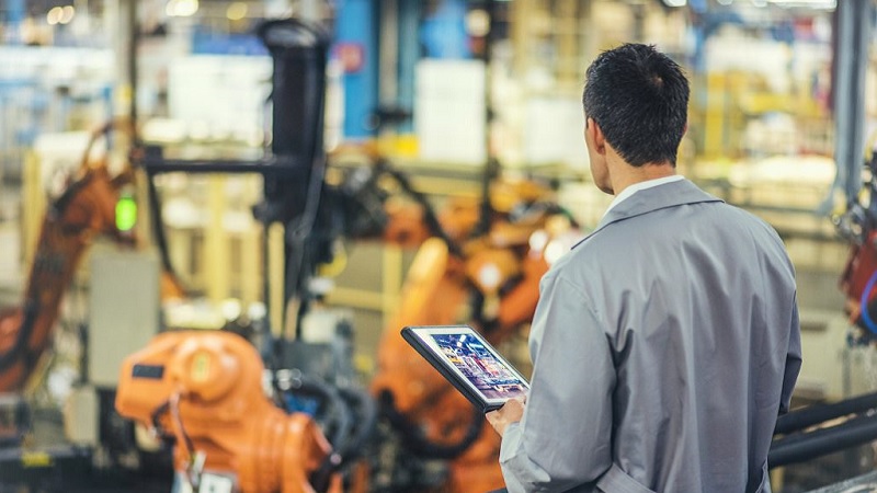 Ein Mechaniker in einer Fabrikhalle h&auml;lt ein Tablet in der Hand