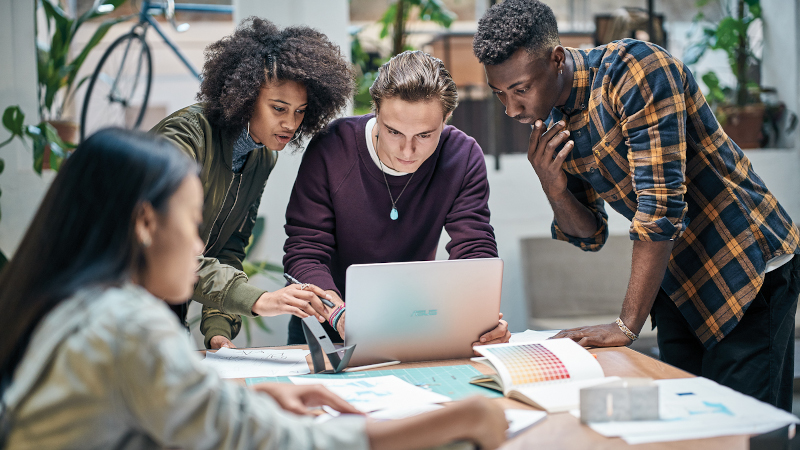Auf dem Bild sind 4 Studenten zu sehen, die miteinander reden und am Computer arbeiten