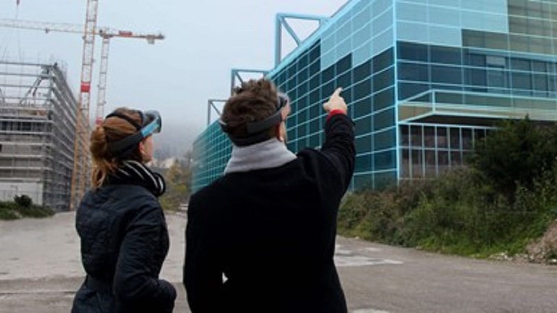 Zwei Menschen schauen mit einer HoloLens auf im Bau befindliche H&auml;user