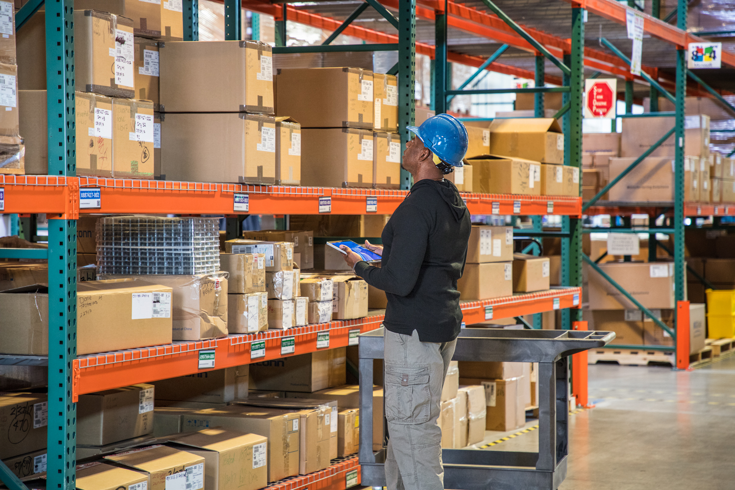 Male worker wearing hardhat using tablet and looking at boxes in warehouse