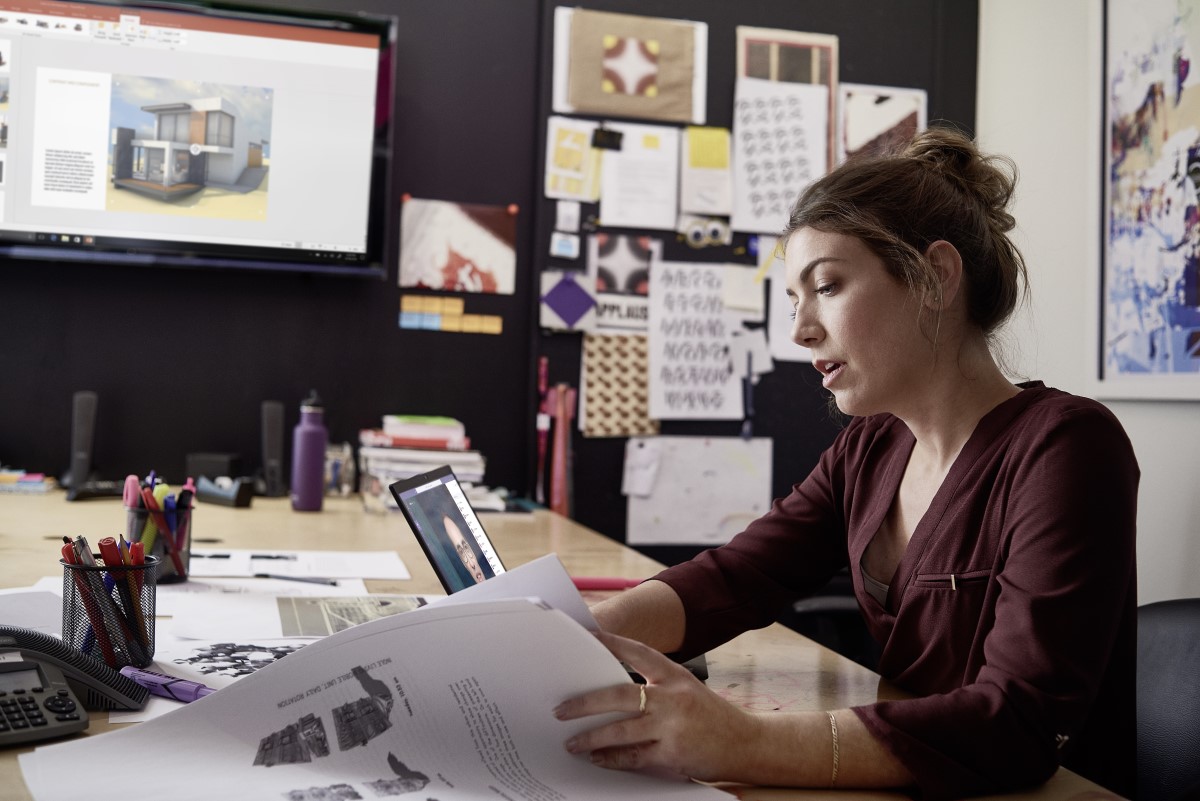Female small business professional working on designs using devices running PowerPoint and Microsoft Teams