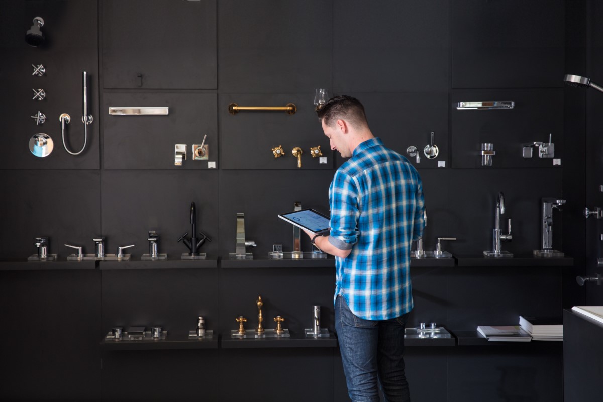 Male millennial using Surface Pro and Surface Pen, standing in front of faucet display wall in a kitchen and bath showroom