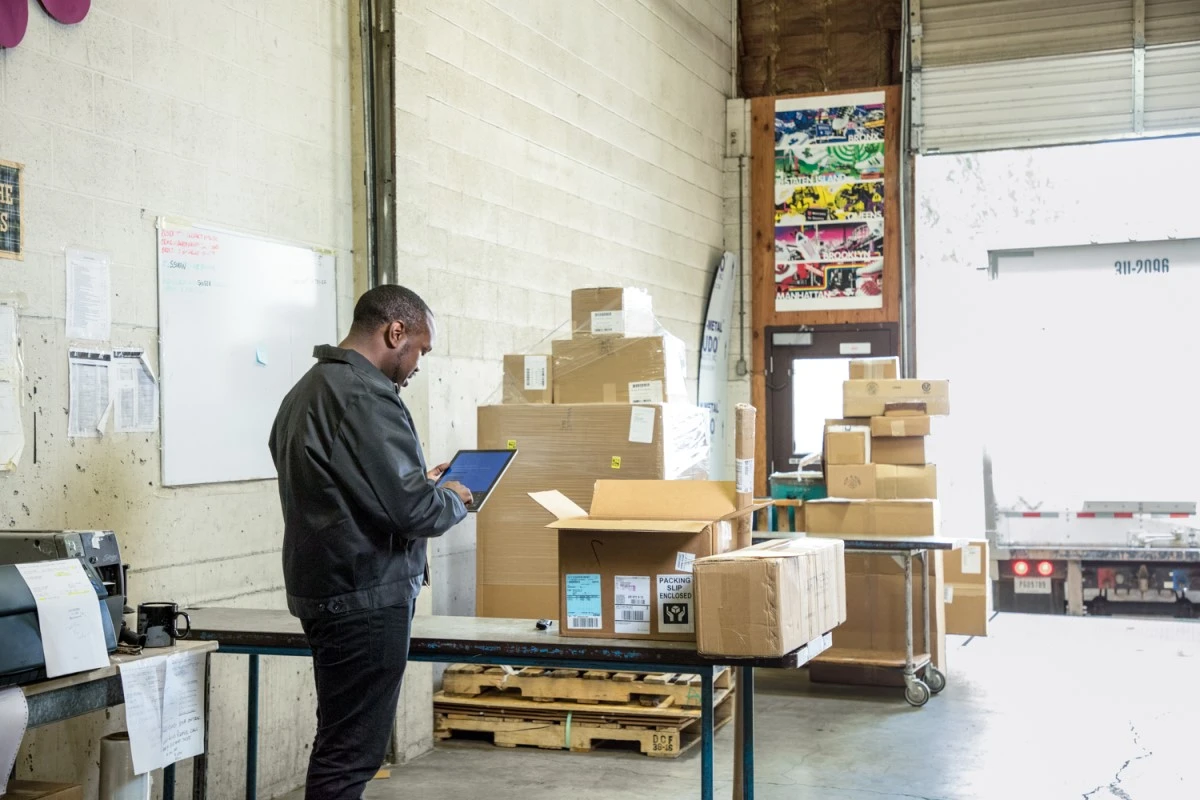 Male employee in warehouse loading dock using Surface Pro. Cardboard packages ready to be loaded on to truck for shipping