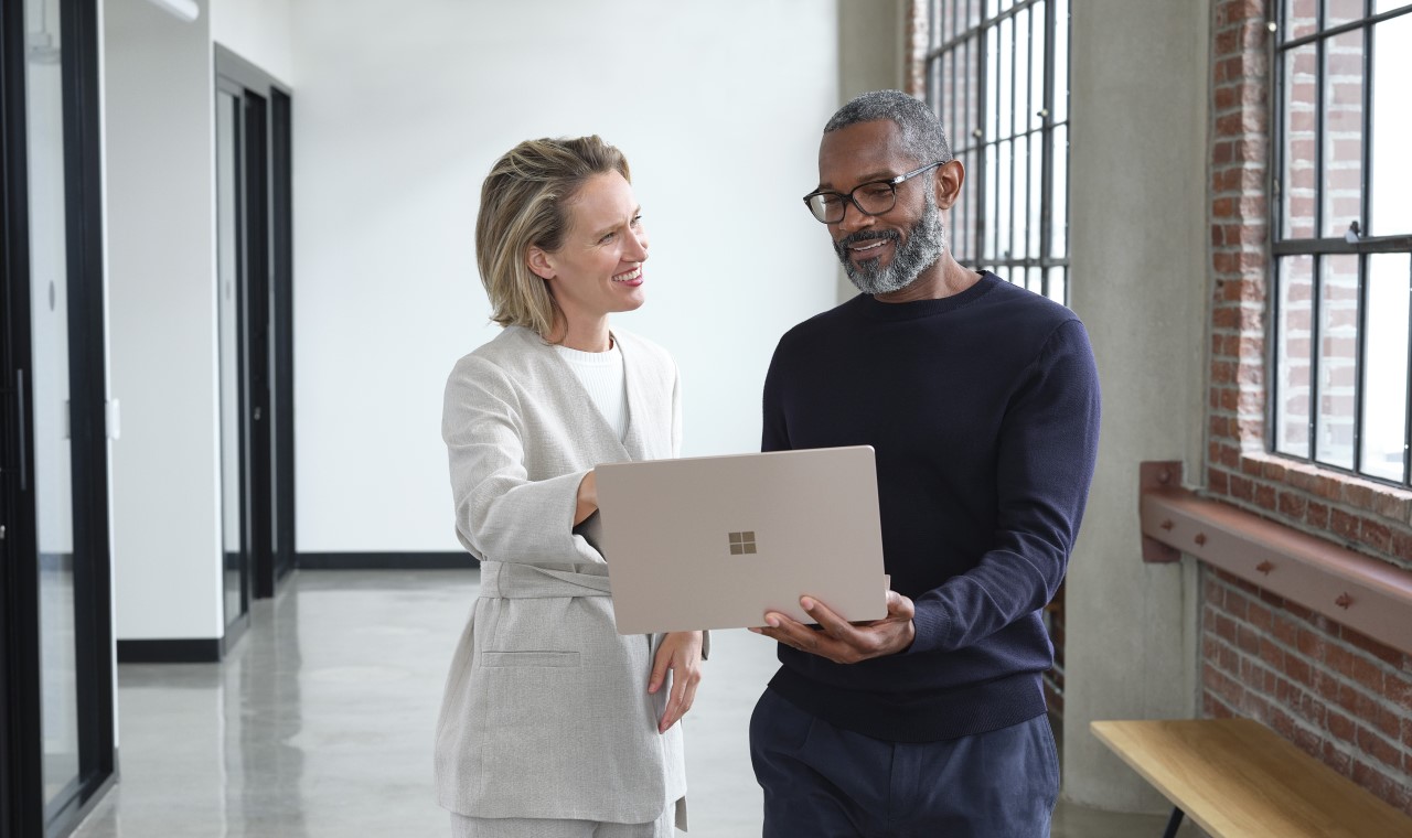 Man and woman standing in an office hallway discussing content on a laptop