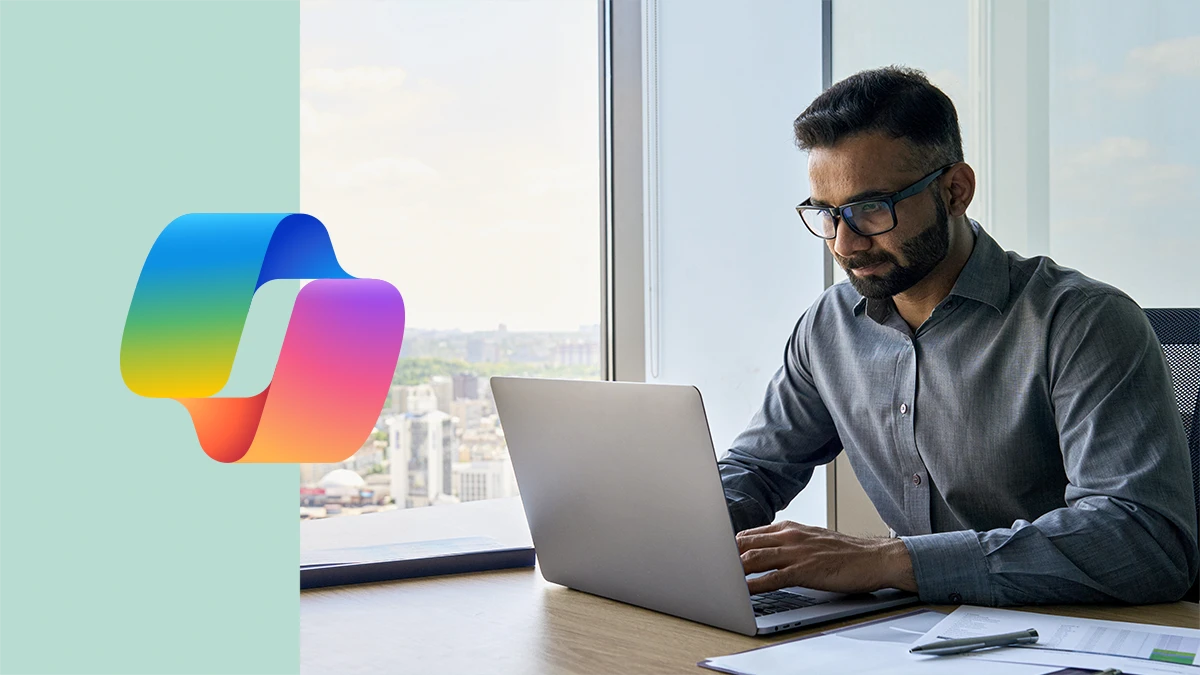 Executive sitting at desk using laptop in an office with a panoramic view. Including Copilot logo