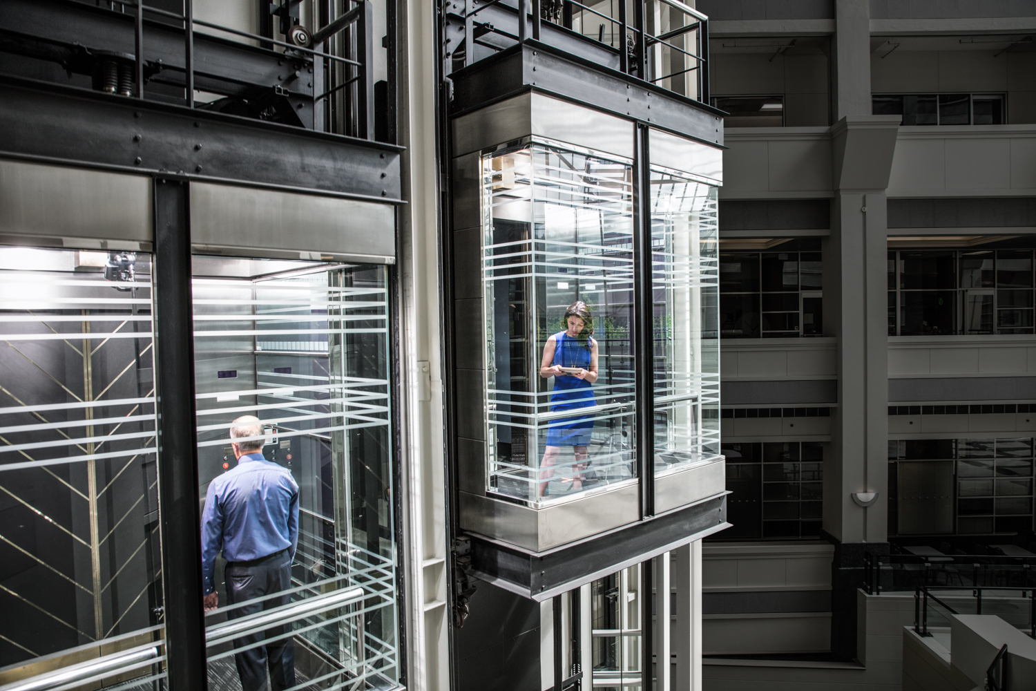 Photo of a business woman and man in separate glass elevators