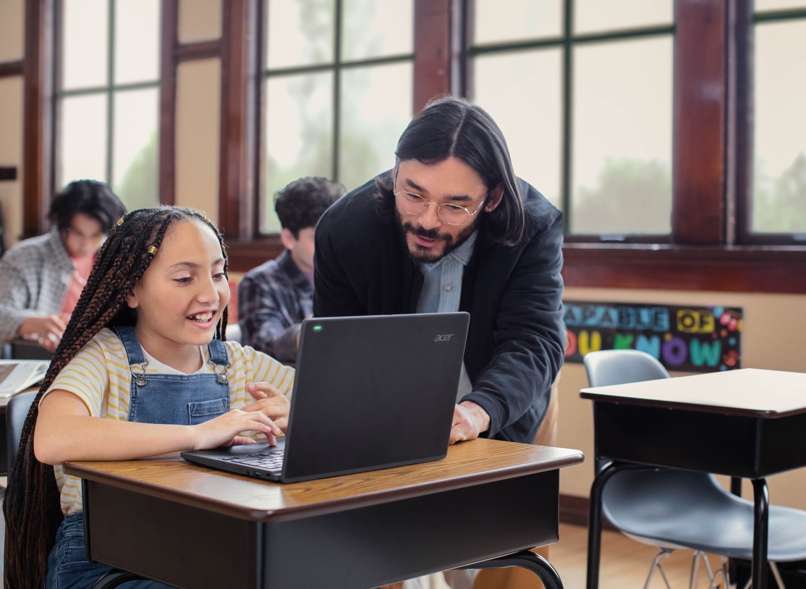 An educator in a classroom helps a student with schoolwork on her laptop