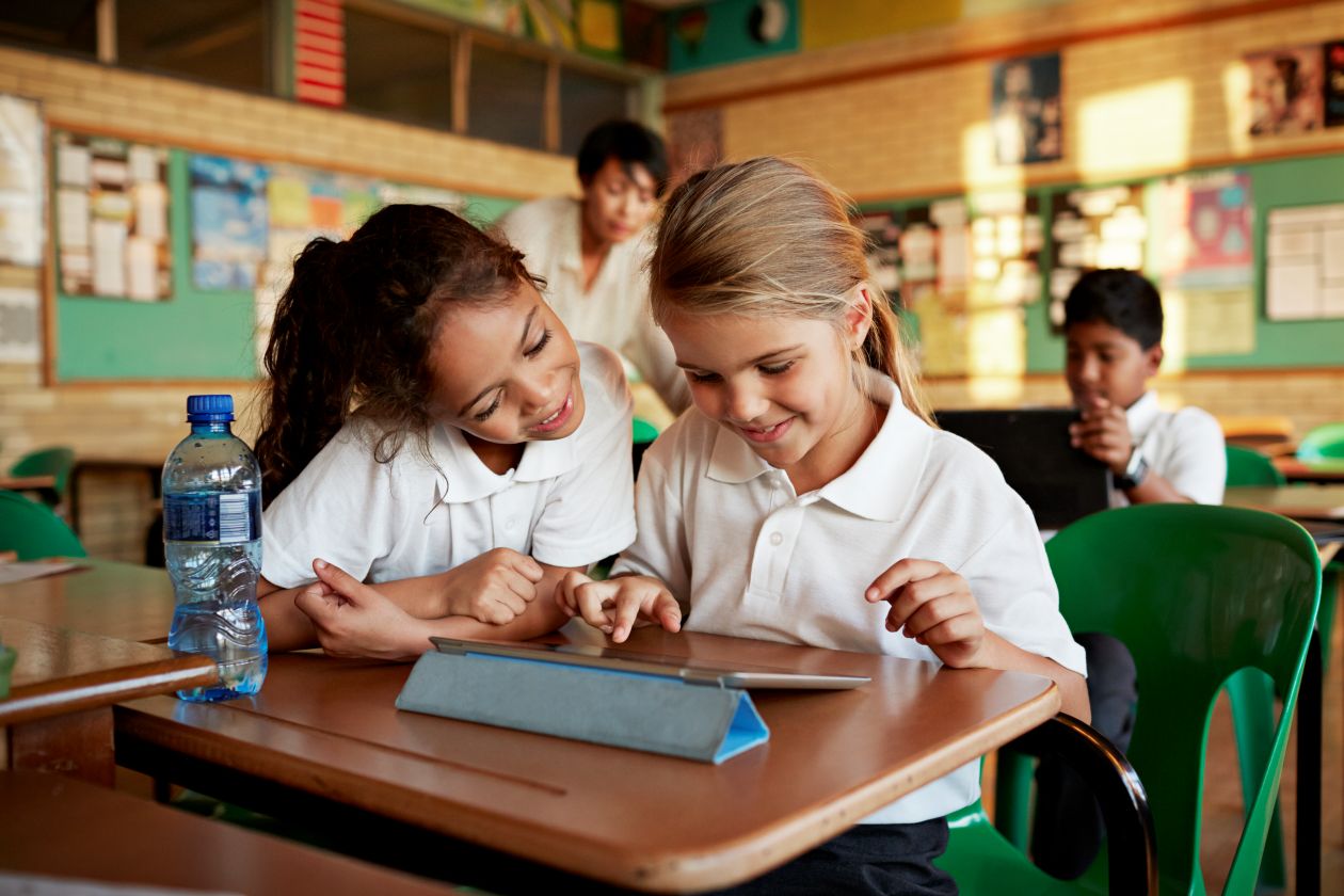 Two young students playing on a tablet in a school classroom