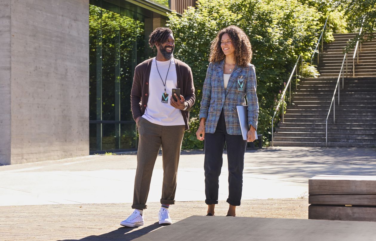 Two higher education leaders walk together outside on a college campus