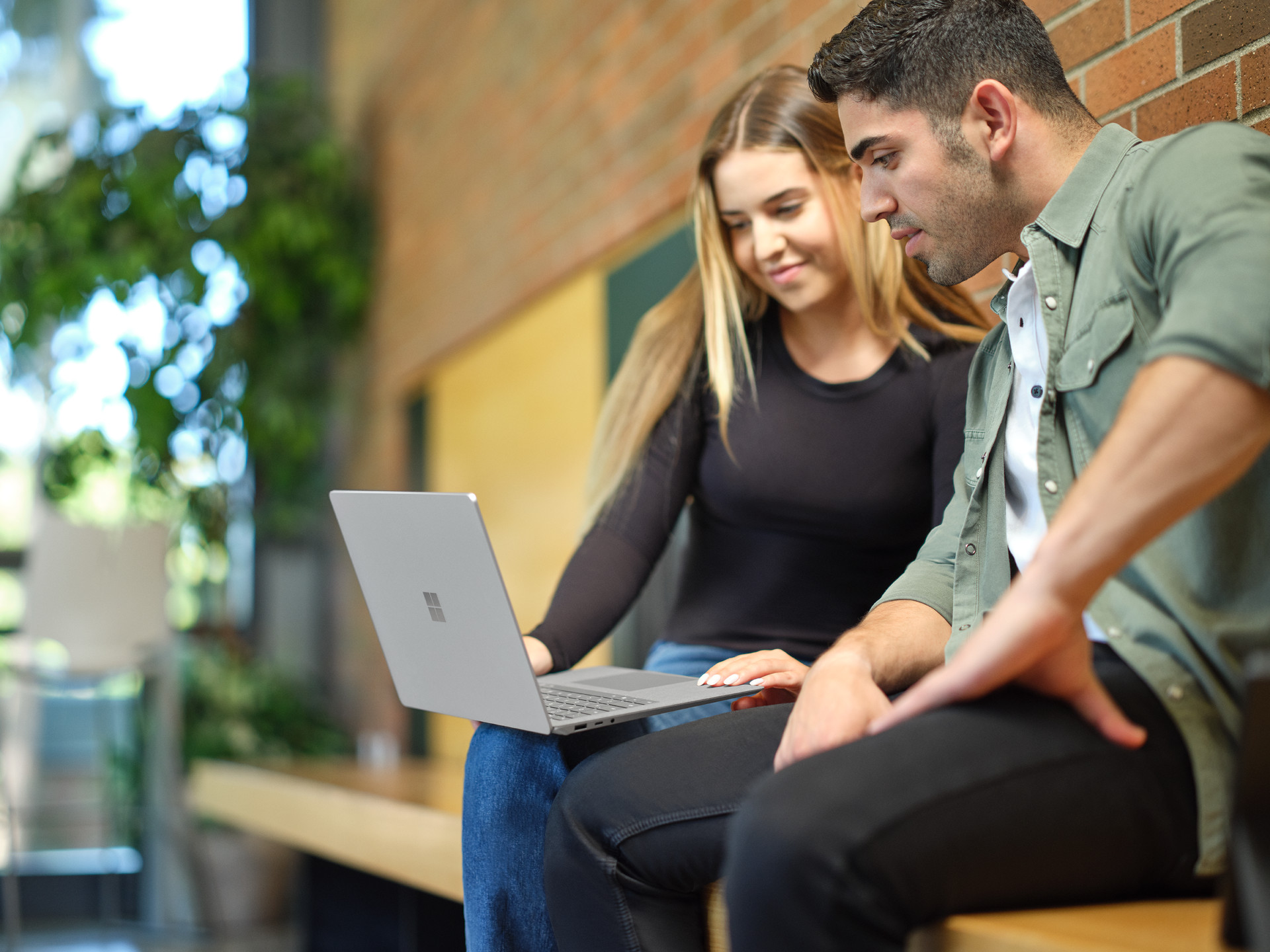 Two people sitting on a bench looking at a laptop together