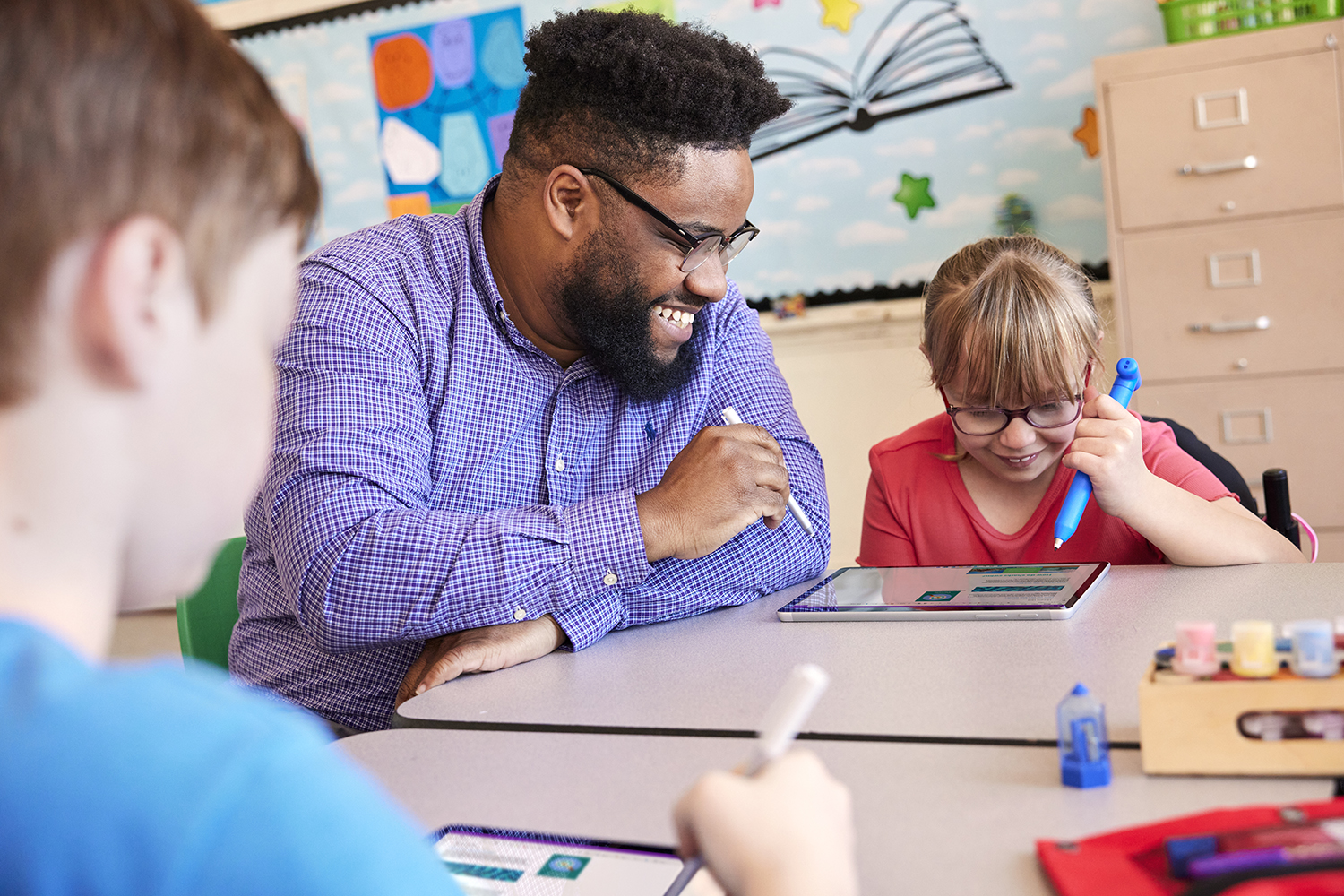 A teacher sitting with students, working together on a tablet