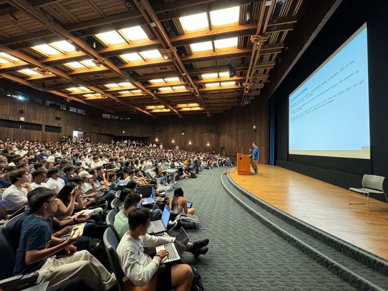 Decorative. A university professor standing at a podium and lecturing to an auditorium full of students