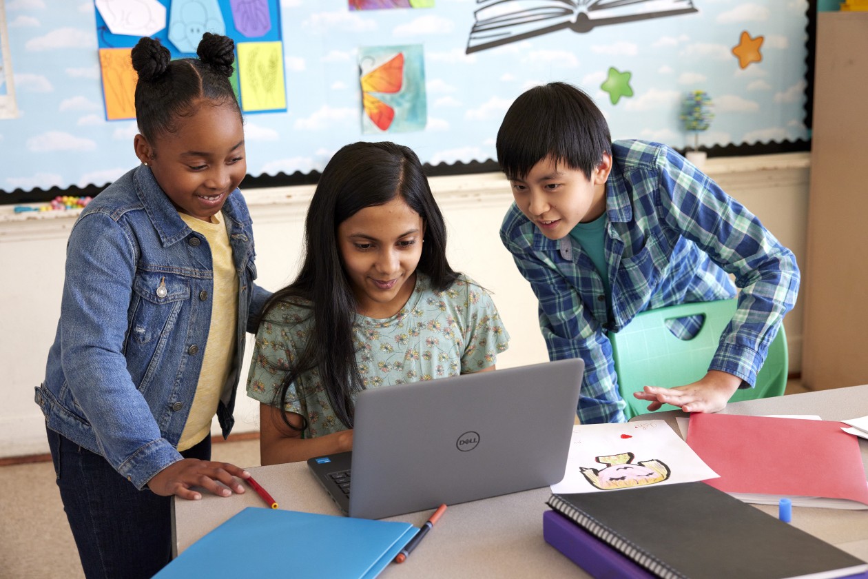 Three students working together on a laptop in a school classroom