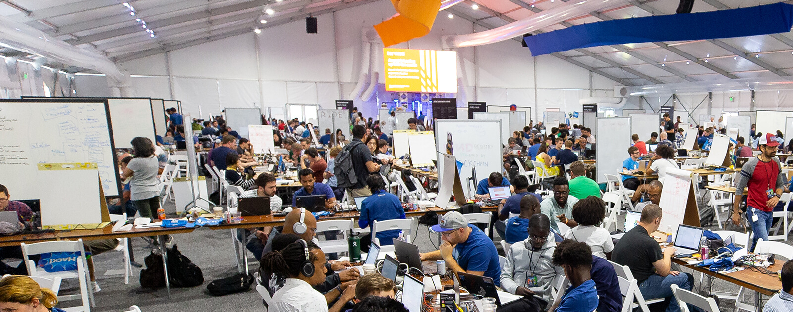 View of a large room packed with coders and others at team workstations during a Hackthon