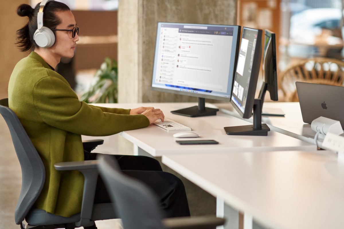 A man collaborating during a Microsoft Teams meeting while working in an open office setting on dual monitor​s
