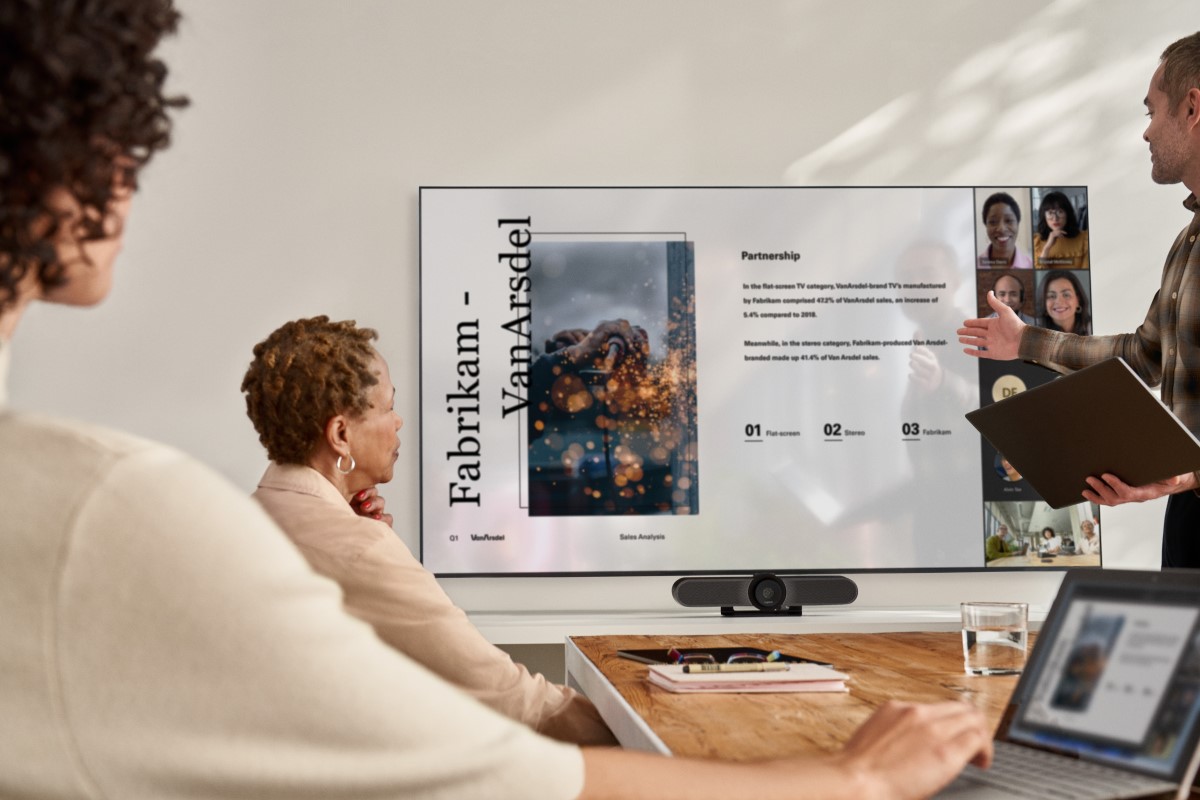 People sharing PowerPoint content via Gallery View in a Microsoft Teams Room meeting while a woman on a laptop has joined in Companion Mode​