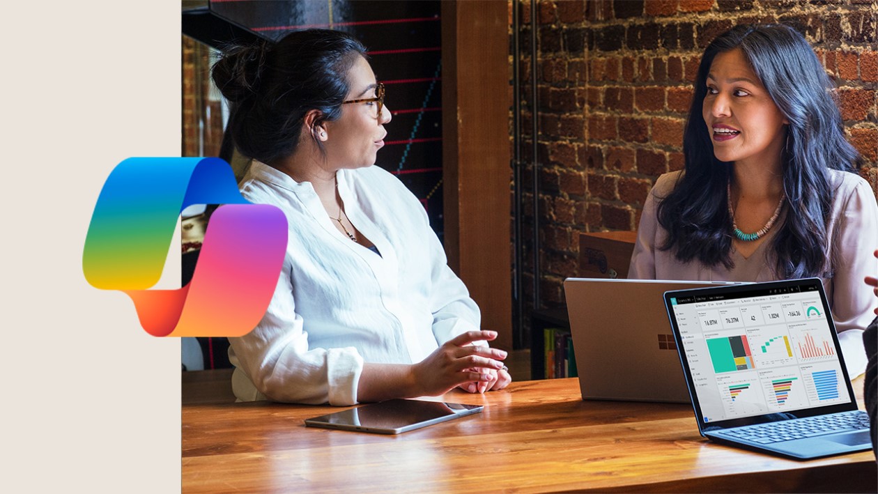 Two people sitting at a table looking at a laptop. Microsoft Copilot logo included