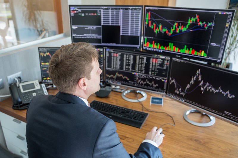 Man in front of three monitors showing charts denoting trading activity