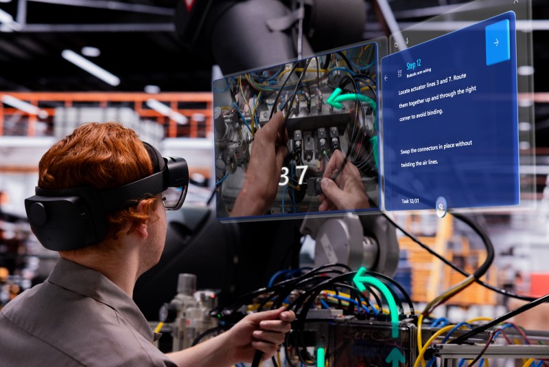 Automotive manufacturing worker in a factory uses a Guide wearing the HoloLens 2 to service a robotic arm wiring system with mixed reality instructions