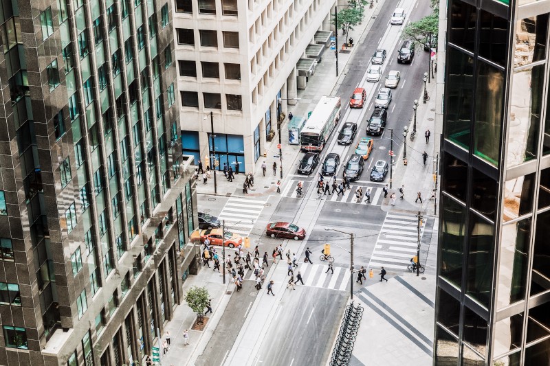 Downtown city street view from high angle inside office building. Large groups of pedestrians walk across street at crosswalk as car traffic flows through stoplight at busy intersection