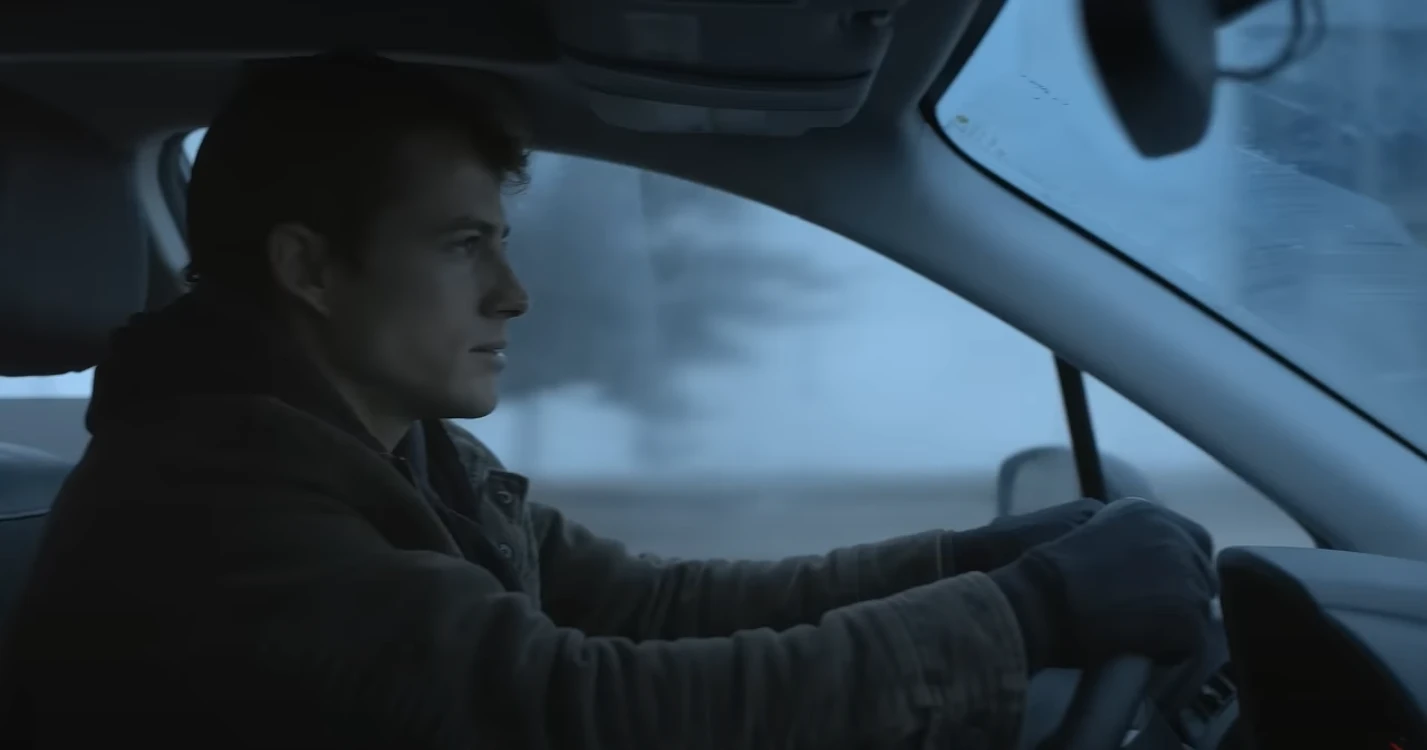 A still-frame from the Microsoft Copilot Game Day Commercial: a man wearing a coat and gloves driving a car in the winter with snow in the background