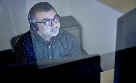 Image of a tech worker wearing headphones, looking at his computer screen
