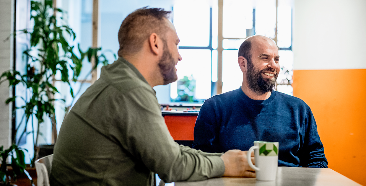 Two workers sit smiling at a table, over a cup of coffee