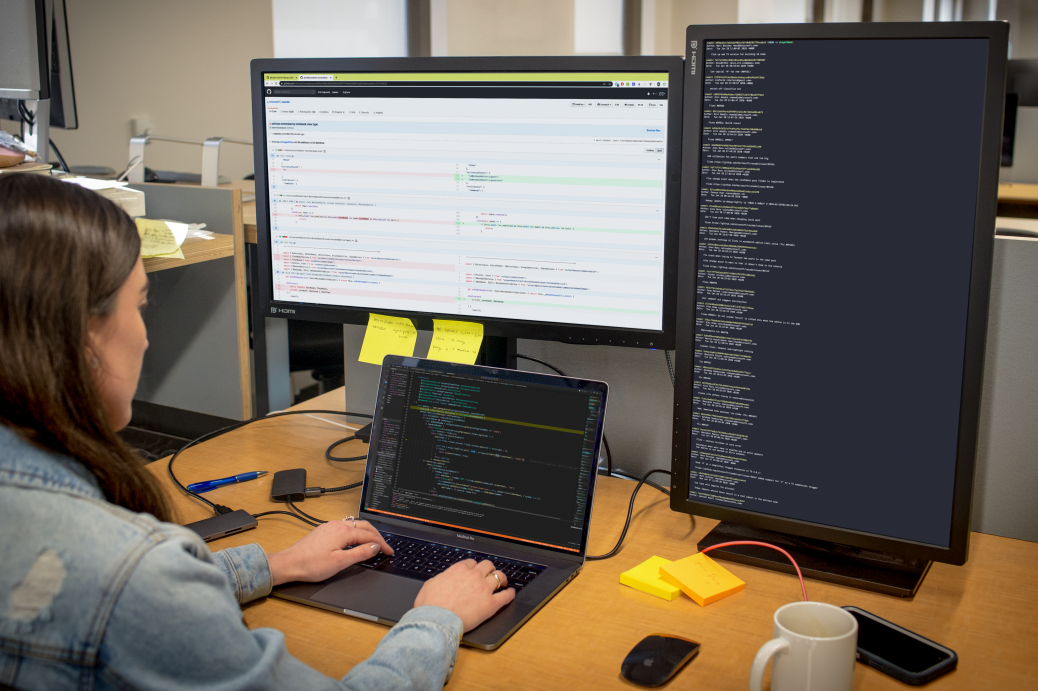 Developer coding at her workspace in an enterprise office using Visual Studio for Mac on a multi-monitor setup