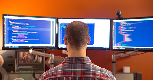 An IT professional working on a multi-screen PC workstation