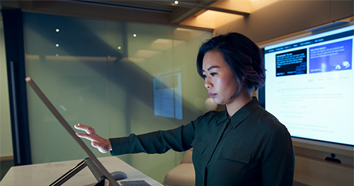 An image of a woman wearing a dark shirt in a dim office scrolling or working on a Microsoft Surface Studio