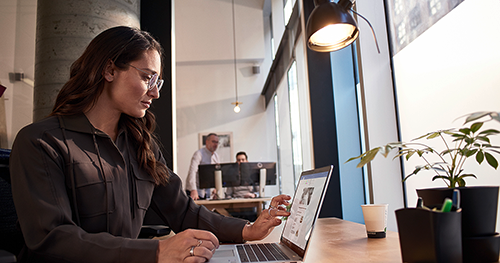An image of a female tech worker sitting at a table working on her laptop