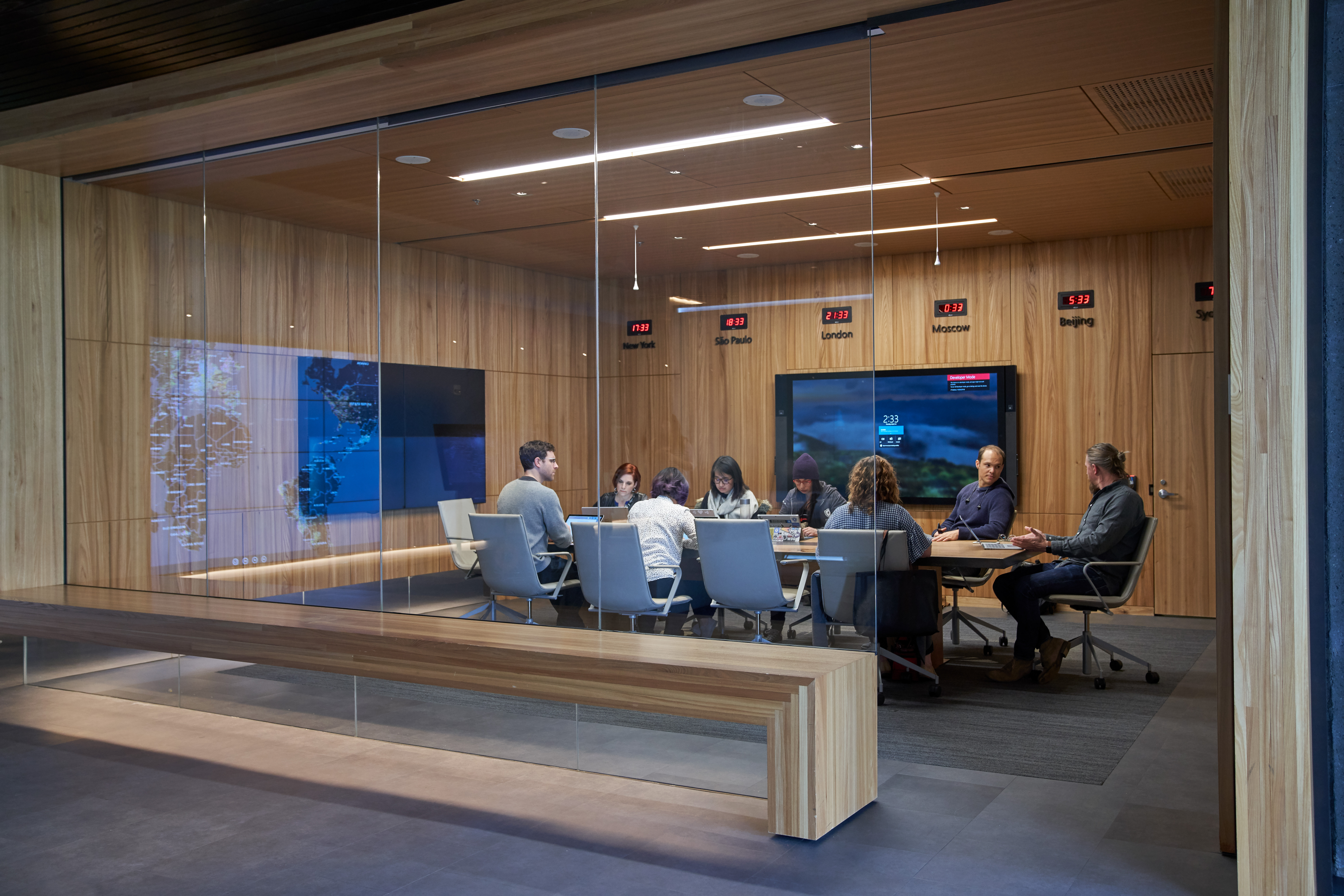 Conference room or board room meeting with people sitting around table in a room with international time clocks, and a map projection/reflection