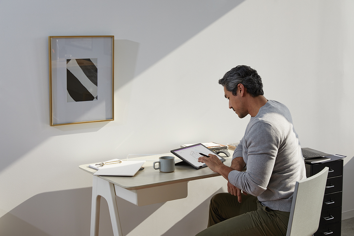 Adult male in home office environment using Microsoft OneNote at a desk with a black Microsoft Surface Pro 7 in studio mode. Black Microsoft Surface Pen in hand