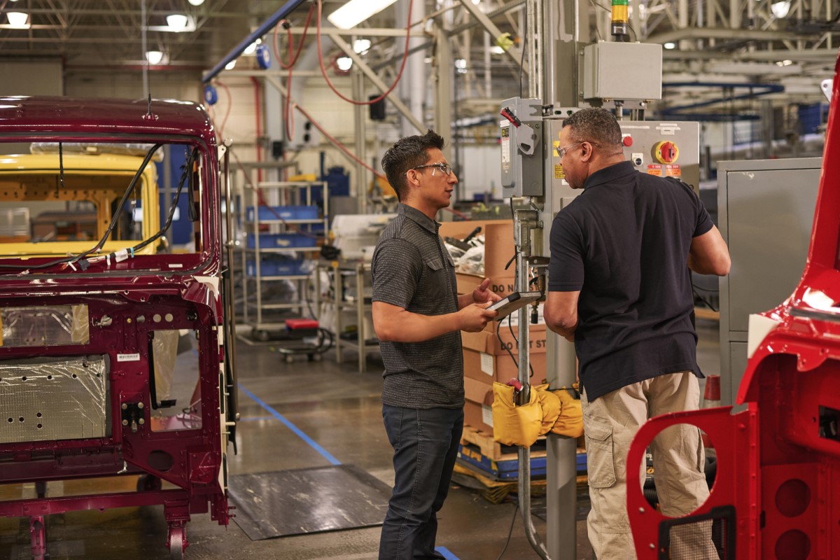 Two engineers wearing safety goggles use machinery at a manufacturing plant