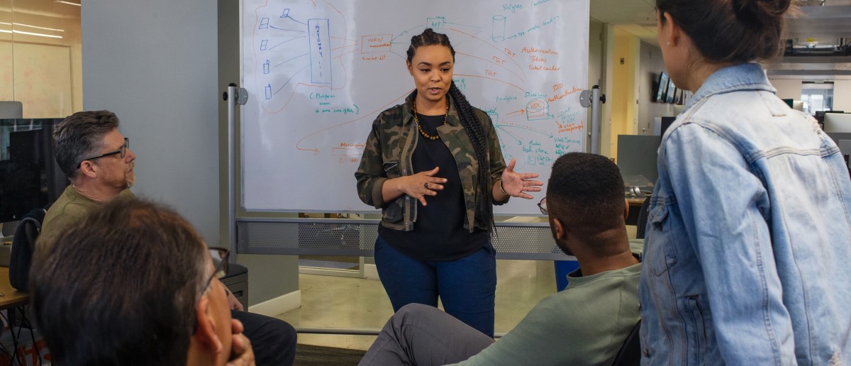 Real people, real offices. Black female developer speaking in front of a white board during team stand up meeting
