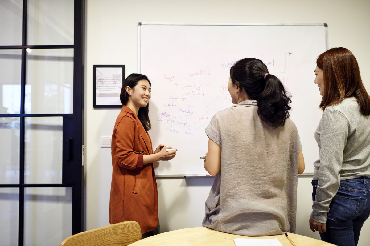 Three women grouped around whiteboard brainstorming ideas