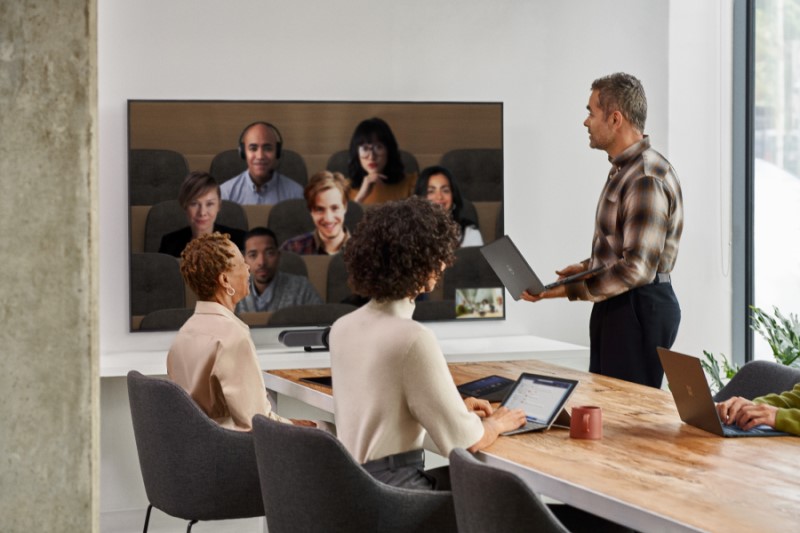 A male speaker presenting in a Microsoft Teams Room meeting while viewing remote participants in Together Mode on the front of room screen​