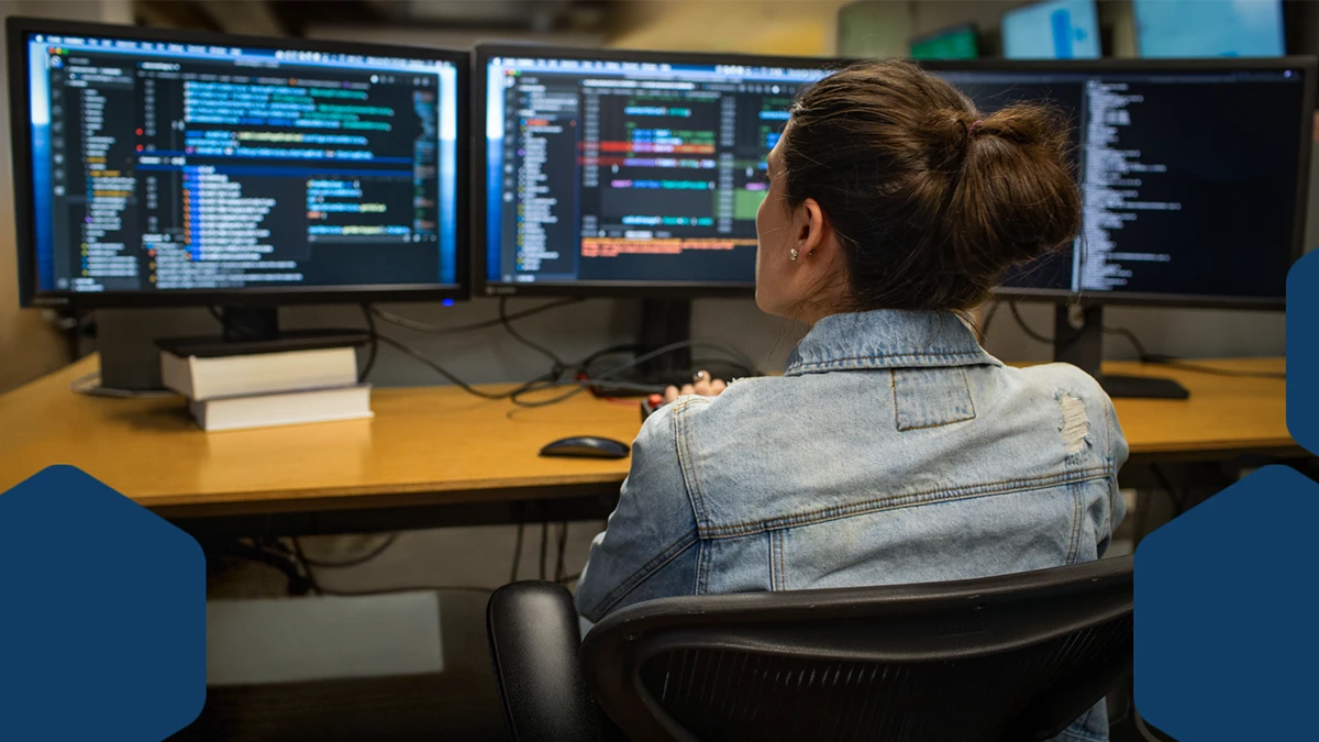 Photo of a developer coding her workspace in an enterprise office, using Visual Studio on a multi-monitor set up