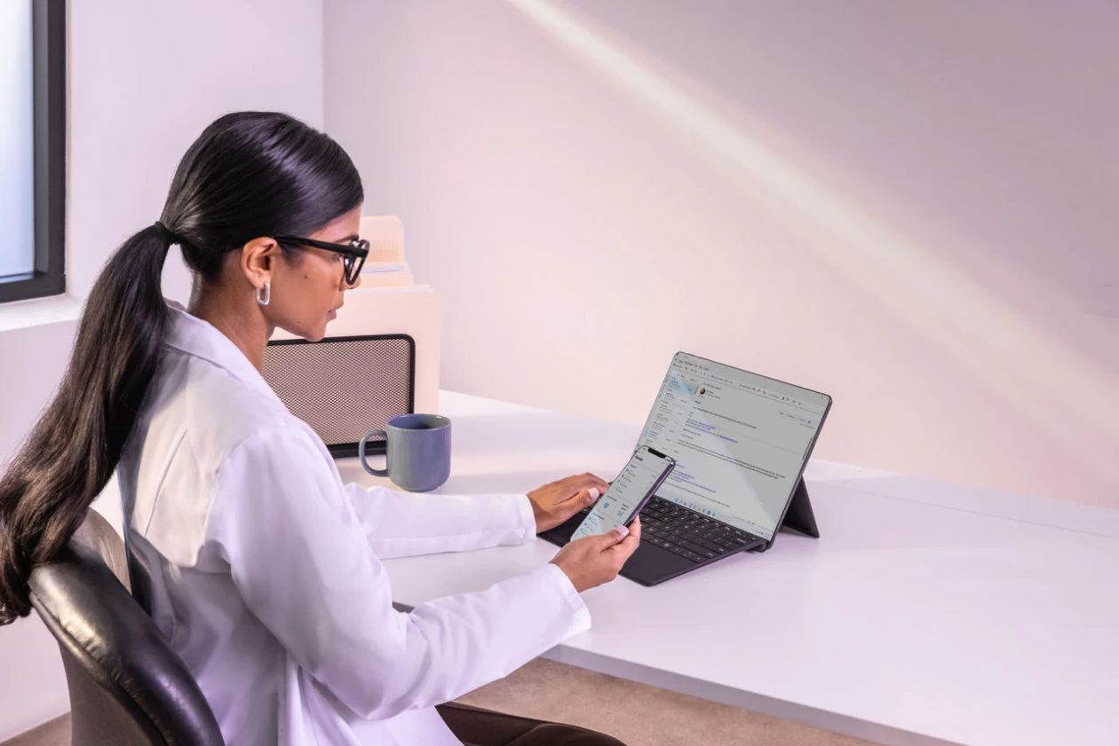 Woman sitting at desk with laptop open and cell phone in hand
