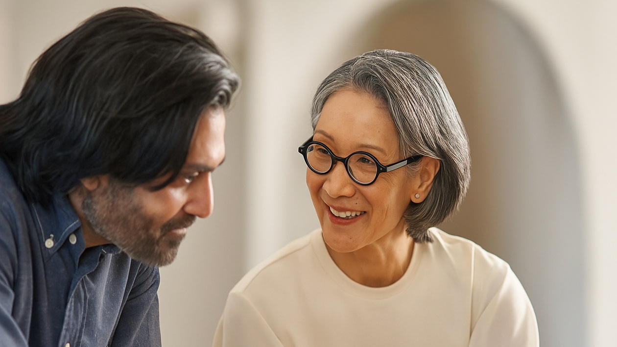 Smiling woman with glasses talking to a man with long hair indoors