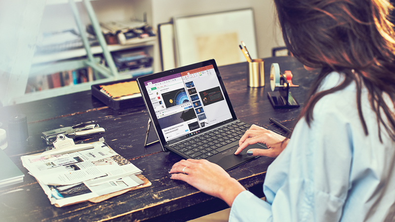 Femme travaillant sur un ordinateur portable, assise &agrave; son bureau dans son bureau &agrave; domicile. Elle a un presse-papiers, du courrier et d&rsquo;autres fournitures sur son bureau et une &eacute;tag&egrave;re en arri&egrave;re-plan
