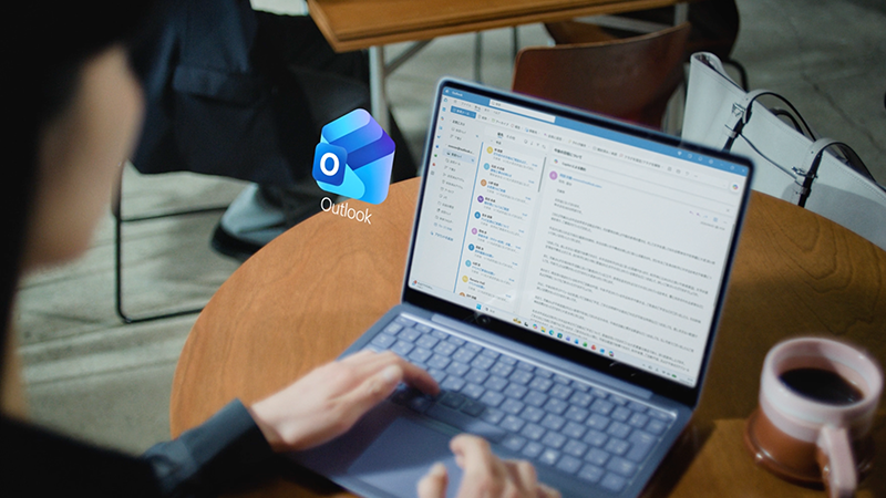 テーブルでノートパソコンのMicrosoft Outlookを使ってメールを下書きしている人